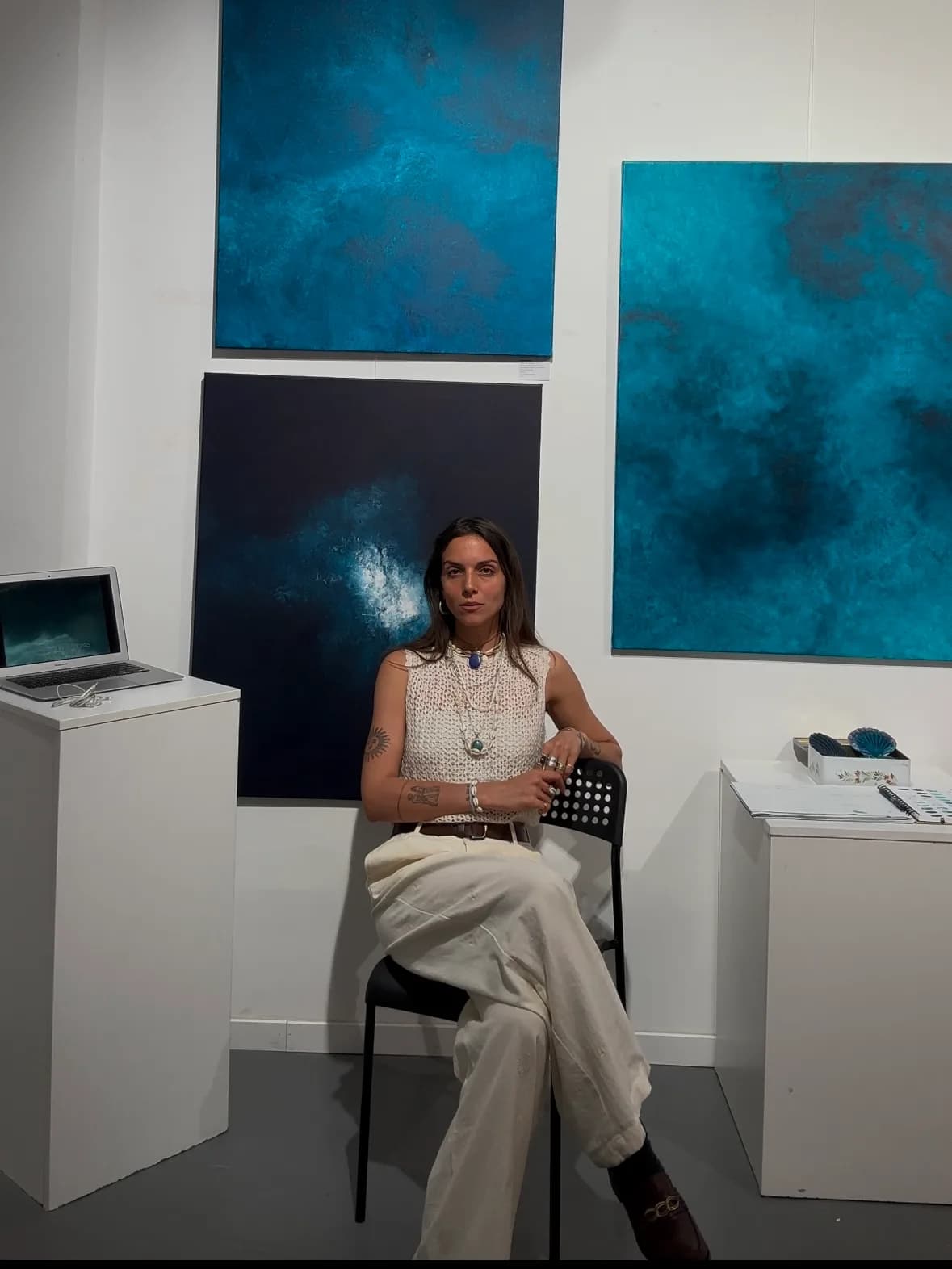 Daphné Mistretta assise devant trois de ses toiles, galerie Kiff & Marais