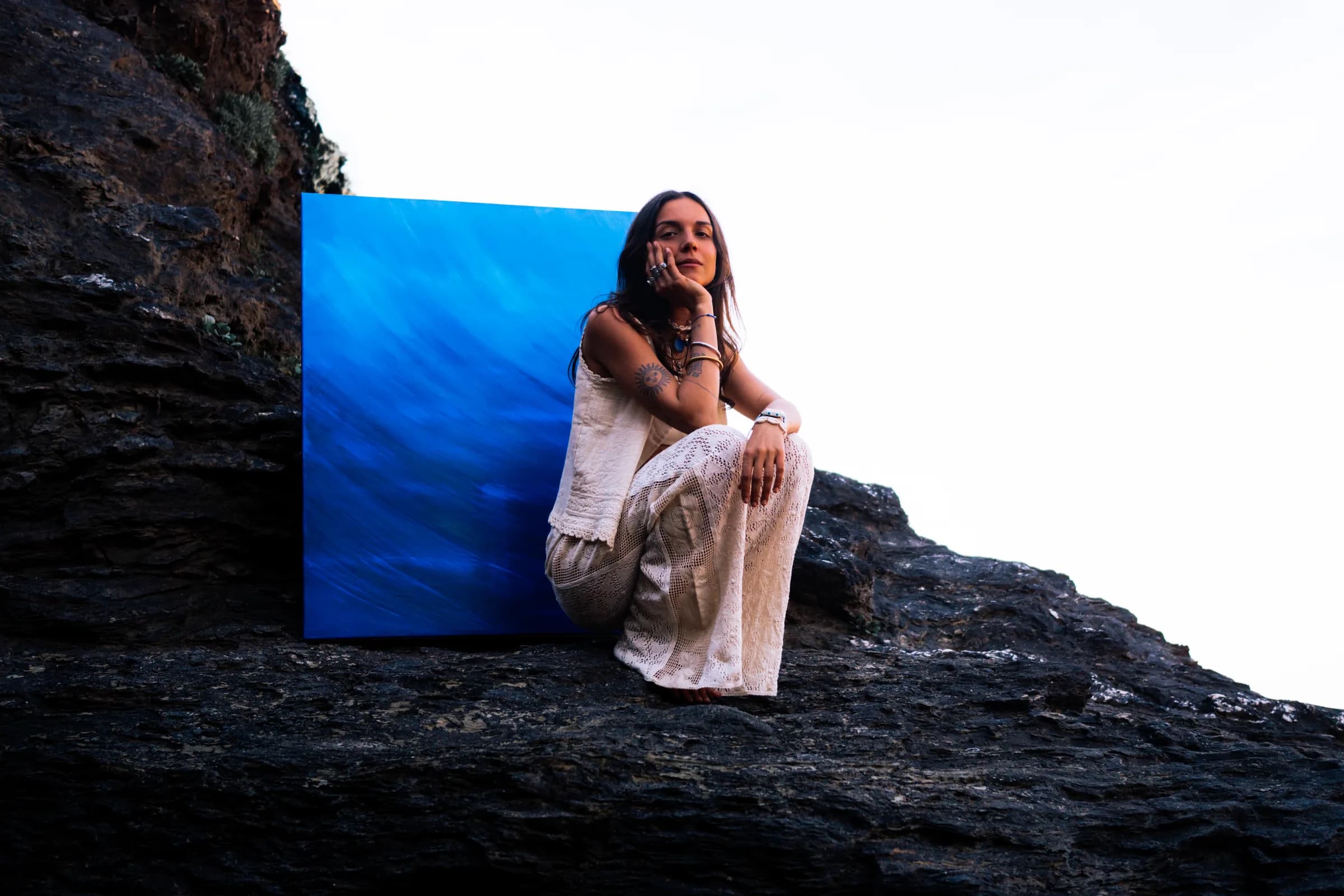 Assise contre la toile bleue, sur le rocher